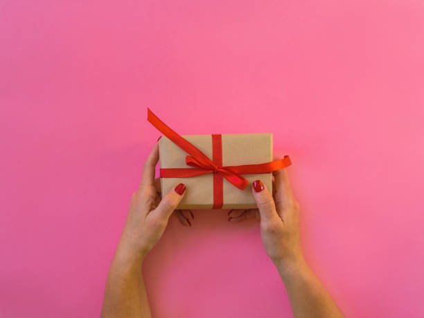 istock Woman hands holding gift, pink background. 1295006389