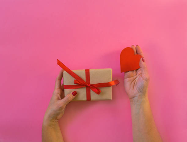 istock Woman hands holding gift and red heart, blue background. 1295007336