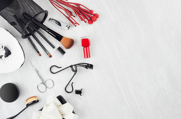 istock Bright black, silver luxury glossy make up accessories, beauty products, manicure tools with red sprig, silver sequins purse on white wood board, top view, border. 1295011244
