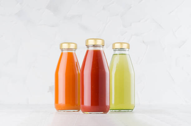 tomate, carotte, jus de légumes verts mis dans des bouteilles en verre avec casquette maquette en rangée sur la table en bois blanc à l’intérieur léger, modèle pour l’emballage, la publicité, le produit de conception, l’image de marque. - tomato juice drink celery juice photos et images de collection