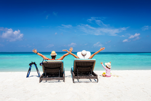 Happy family on sunbeds enjoys their vacation on a tropical beach with turquoise ocean and sunshine