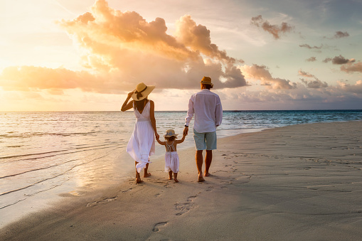 Una familia camina de la mano por una playa tropical paradisíaca durante la puesta del sol photo