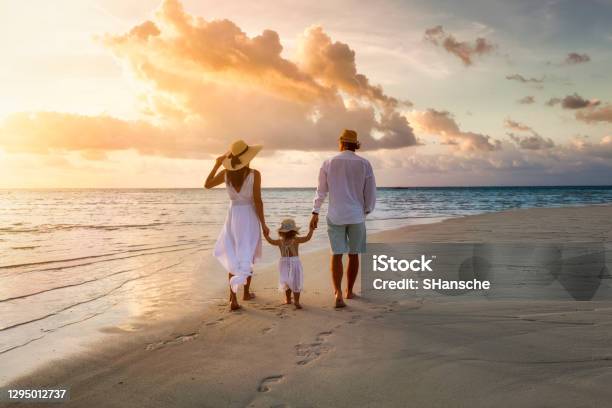 A Family Walks Hand In Hand Down A Tropical Paradise Beach During Sunset Stock Photo - Download Image Now