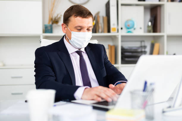istock Businessman in face mask working on laptop 1295012746