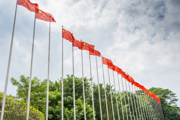 A row of Chinese National flags being hoisted up the flagpole against cloudy sky in the park stock photo