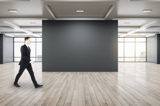 istock Businessman walking in gallery interior with empty black wal 1295018471