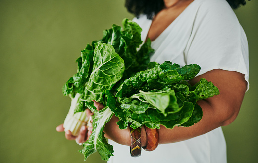 Studio shot of a young woman holding a bunch of spinach against a green background