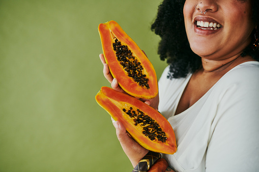 Studio shot of a woman holding papaya against a green background
