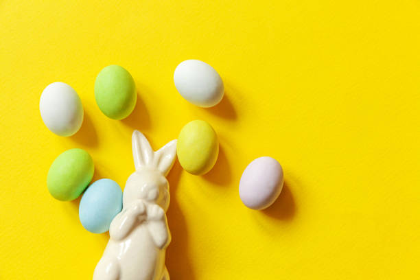 istock Happy Easter concept. Preparation for holiday. Easter candy chocolate eggs sweets and bunny toy isolated on trendy yellow background. Simple minimalism flat lay top view copy space 1295027173