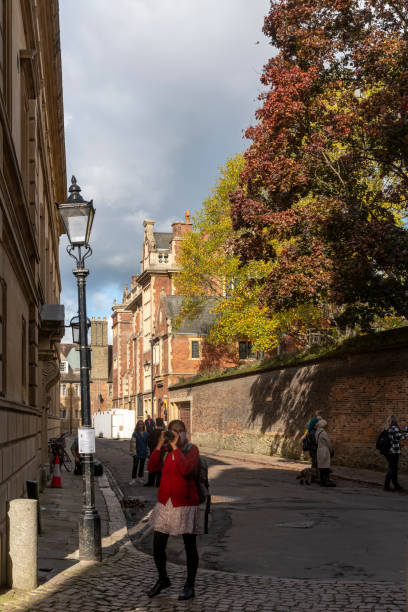 An Asian tourist or student taking a photograph of King's College Chapel from Trinity Lane with Clare College on the left. Cambridge, England, UK.