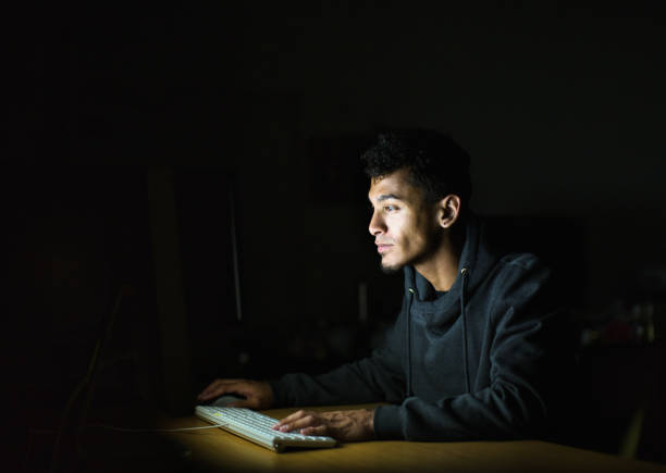 Young man concentrates as he works late, illuminated by glowing computer screen