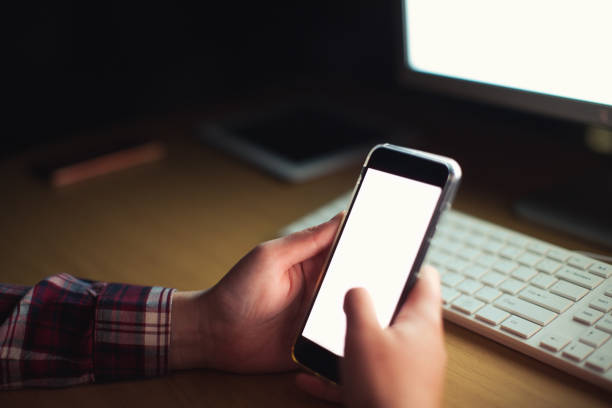 istock Young woman working late multitasks on her cellphone, illuminated by glowing computer screen 1295031499