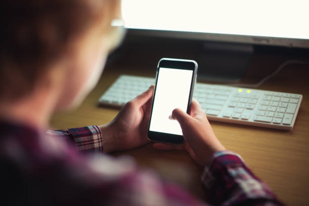 istock Young woman working late multitasks on her cellphone, illuminated by glowing computer screen 1295033114