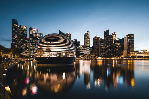 Apple opened the worlds first floating Apple Store at the Marina Bay in Singapore at the time of this shoot, 10th September, 2020. After a few days it has already become a Singapore landmark. Here the store seen at sunset. Behind the store the skyline of the Singapore financial district.