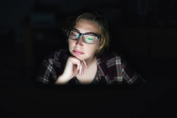 istock Young woman looks thoughtful as she works late, illuminated by glowing computer screen 1295036362