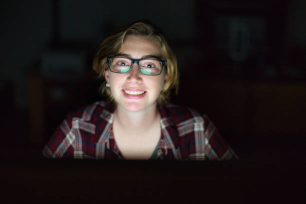 istock Cheerful young woman working late illuminated by glowing computer screen 1295037366