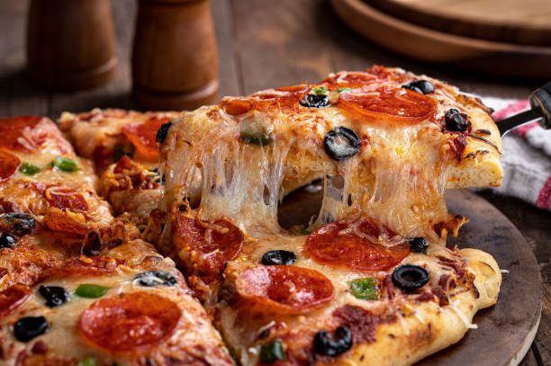 Pizza With Pepperoni, Olives and Peppers Slice of pizza with pepperoni, olives and green peppers on a serving utensil.  Closeup of a cheese pull pizza stock pictures, royalty-free photos & images