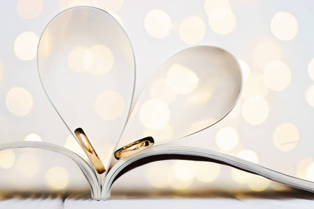 Heartshaped magazine sheets with wedding rings and bokeh effect. stock photo