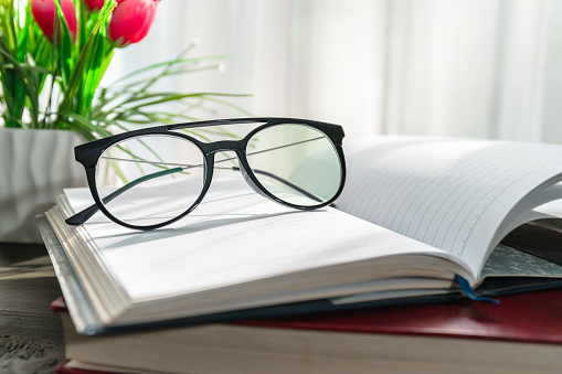Reading glasses put on open books over wooden table beside the window