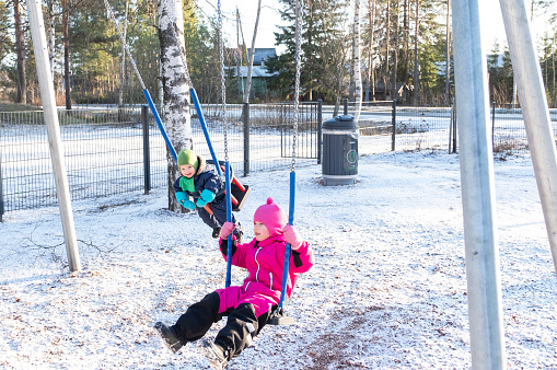 Children play in the playground in winter. A boy and a girl, Caucasians, swing on a children's swing.