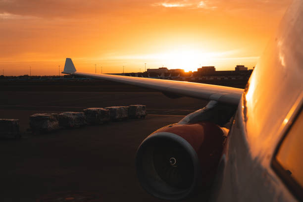 A big commercial airplane as seen from the cockpit window rearwards as the sun sets in the horizon right over the right wing and engine.