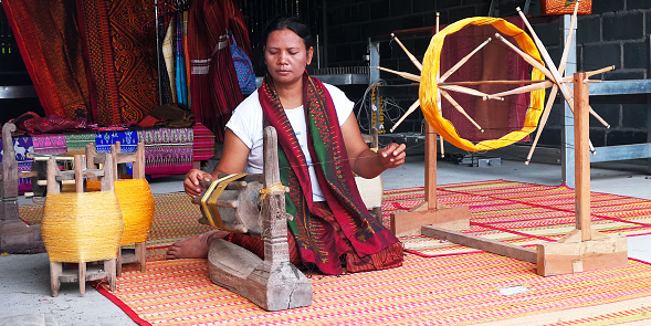 Surin, Thailand - July 27, 2018: Native female in the northeastern countryside is demonstrating the traditional procedure of silk-spinning with yellow silk threads by an old-fashioned wooden machine.