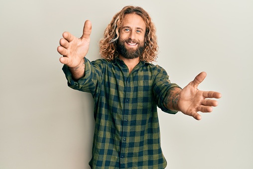 Handsome man with beard and long hair wearing casual clothes looking at the camera smiling with open arms for hug. cheerful expression embracing happiness.