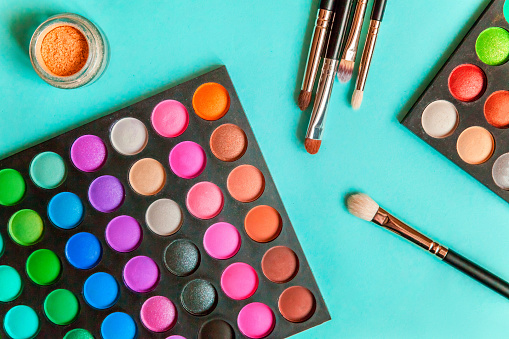 Tools for makeup and cosmetics different shades of eyeshadow palette and make up brush on trendy colorful blue pastel background. Top view flat lay and picturesque