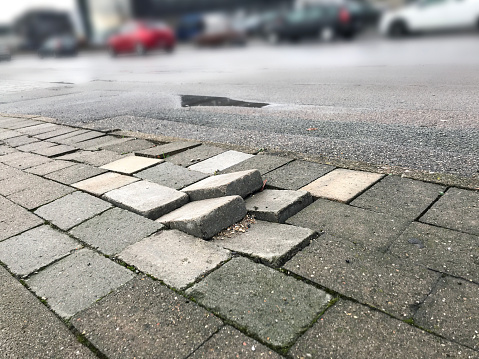 Sidewalk pavement tiles for pedestrians are uneven due to lack of maintenance can cause danger for pedestrians and traffic