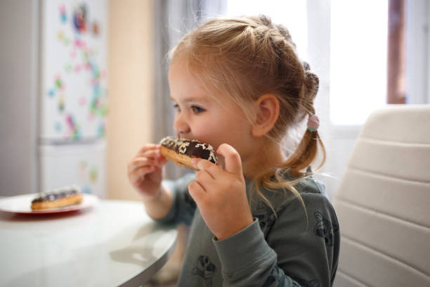 istock little cute girl eating cake while sitting at the kitchen table 1295053882