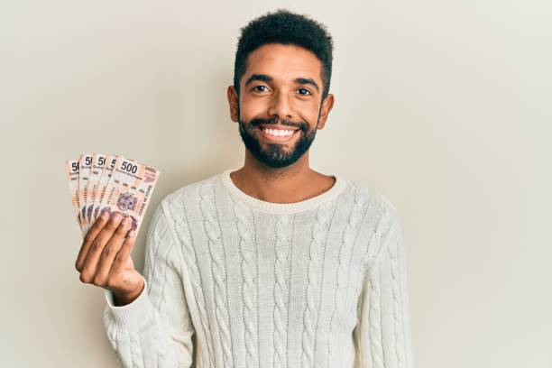 istock Handsome hispanic man with beard holding 500 mexican pesos banknotes looking positive and happy standing and smiling with a confident smile showing teeth 1295056023