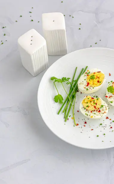 Boiled Eggs on a White Dish Garnished with Black Pepper, Chili Flakes, Salt and Chives Directly Above  Photo