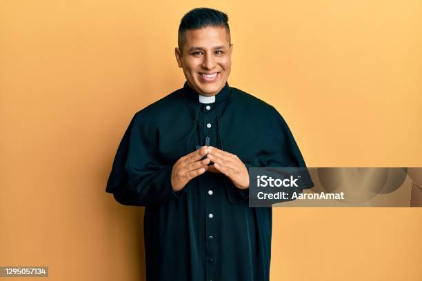 Young Latin Priest Man Standing Over Yellow Background Hands Together And Fingers Crossed Smiling Relaxed And Cheerful Success And Optimistic Stock Photo - Download Image Now