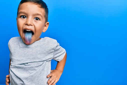 Adorable latin toddler showing blue tongue standing over isolated background.