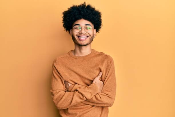 joven hombre afroamericano con pelo afro usando suéter casual de invierno cara feliz sonriendo con los brazos cruzados mirando a la cámara. persona positiva. - adulto joven fotografías e imágenes de stock