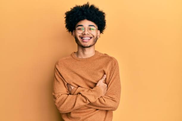 jeune homme afro-américain avec le cheveu afro utilisant le visage heureux occasionnel de chandail d’hiver souriant avec les bras croisés regardant l’appareil-photo. personne positive. - only young man photos et images de collection