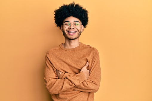 Young african american man with afro hair wearing casual winter sweater happy face smiling with crossed arms looking at the camera. positive person.