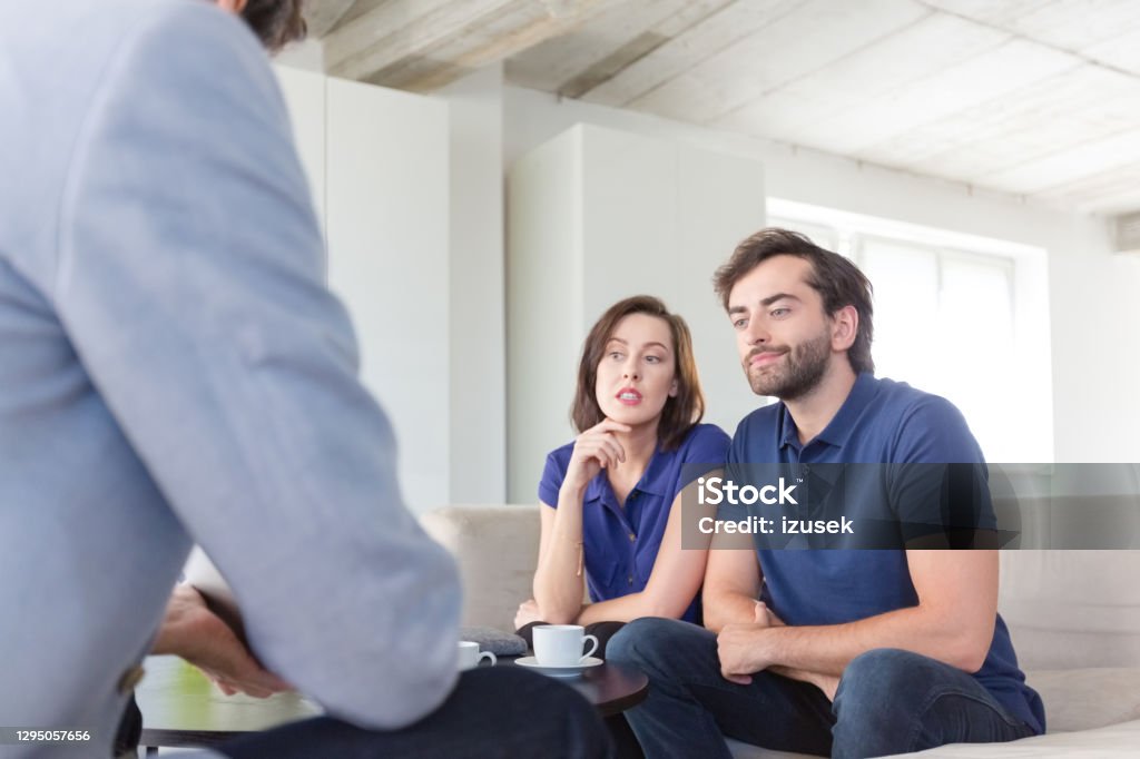 Couple discussing problems with psychotherapist Mid adult couple discussing problems with psychotherapist sitting in living room. They are in meeting at home. 30-39 Years Stock Photo