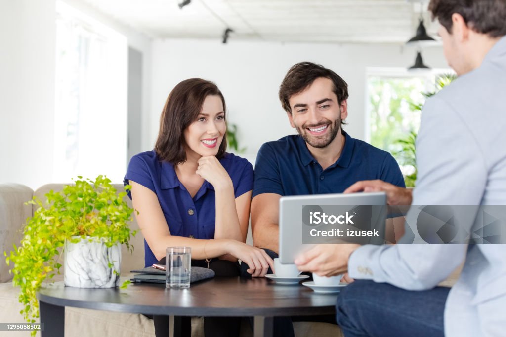 Couple discussing with financial advisor Mid adult couple having meeting with financial advisor or insurance agent at home, sitting on sofa in living room. Financial Advisor Stock Photo