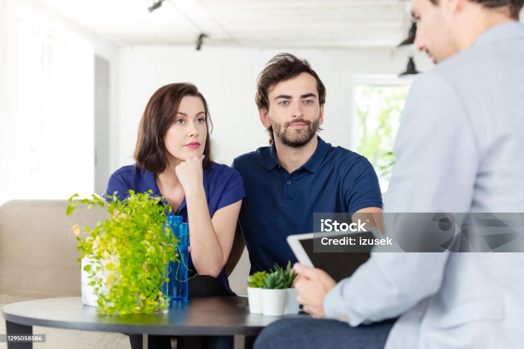 Couple discussing with financial advisor Worried mid adult couple having meeting with financial advisor or insurance agent at home, sitting on sofa in living room. Real Estate Stock Photo