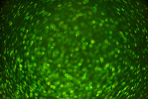 Blurred defocused bokeh background. Texture of green black shamrocks quatrefoil for good luck. Template for St. Patrick's holiday greeting cards. Abstraction template. Copy space Layout for decoration