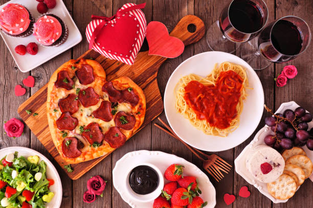 istock Valentines Day dinner table scene on dark wood with heart shaped pizza, pasta, wine, cheese plate and desserts 1295063459