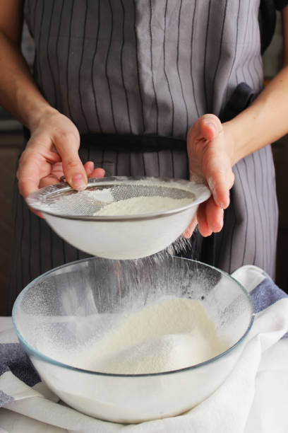 ménage. les mains d’une femme tamiser la farine avec un tamis sur un grand bol pour faire des gâteaux faits maison. - saupoudreuse à farine photos et images de collection