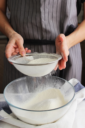 Household. A woman's hands sift flour with a sieve over a large bowl for making homemade cakes. Close up.