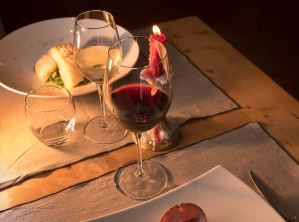 Red wine glass with white wine glass on rustic trattoria table set with red candle lit in candlestick, text space