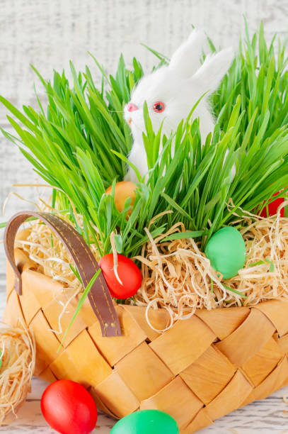 istock Easter basket with green grass filled with brightly colored Easter eggs and White little bunny. Happy Easter. 1295067590