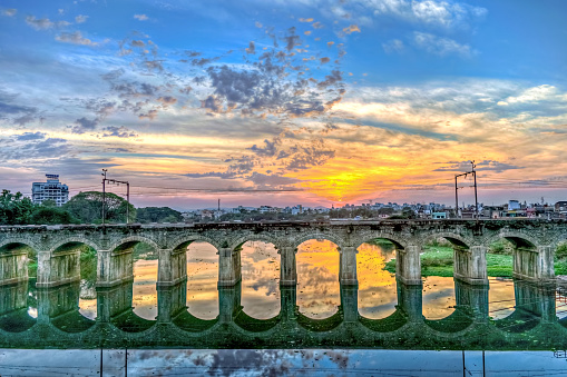 Beautiful Sunset behind an old stone arched rail bridge reflection and nice sky colors background.