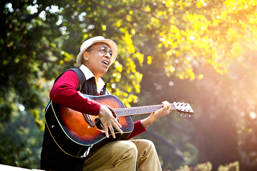 Senior man playing guitar while singing at park