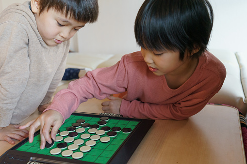 Play in the house.\nA Japanese child is playing game in the house.\nTheir expressions are serious.\nA girl and a boy. Stay Home.