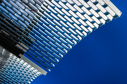 Looking up at a modern metal rooftop canopy outdoors in a public park 
creating abstract shapes against a vibrant blue sky